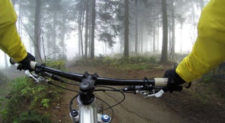 Write with anecdotes: write with impact. Picture is taken from a cyclists point of view, showing the handlebars of a mountain bike.