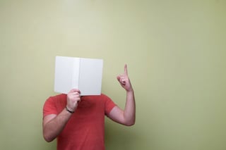 Write with anecdotes: how to make your writing as large as life. Picture shows man holding book up to face and gesturing with his left hand to indicate that he is speaking.
