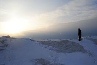 Write with anecdotes: write bigger. Picture shows someone standing on top of a snow drift looking into the sunset.