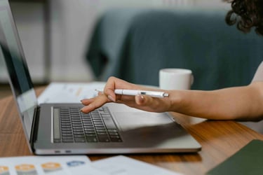 A side view of a laptop open on a desk. A hand holding a pen is hovering over the keyboard ready to type.