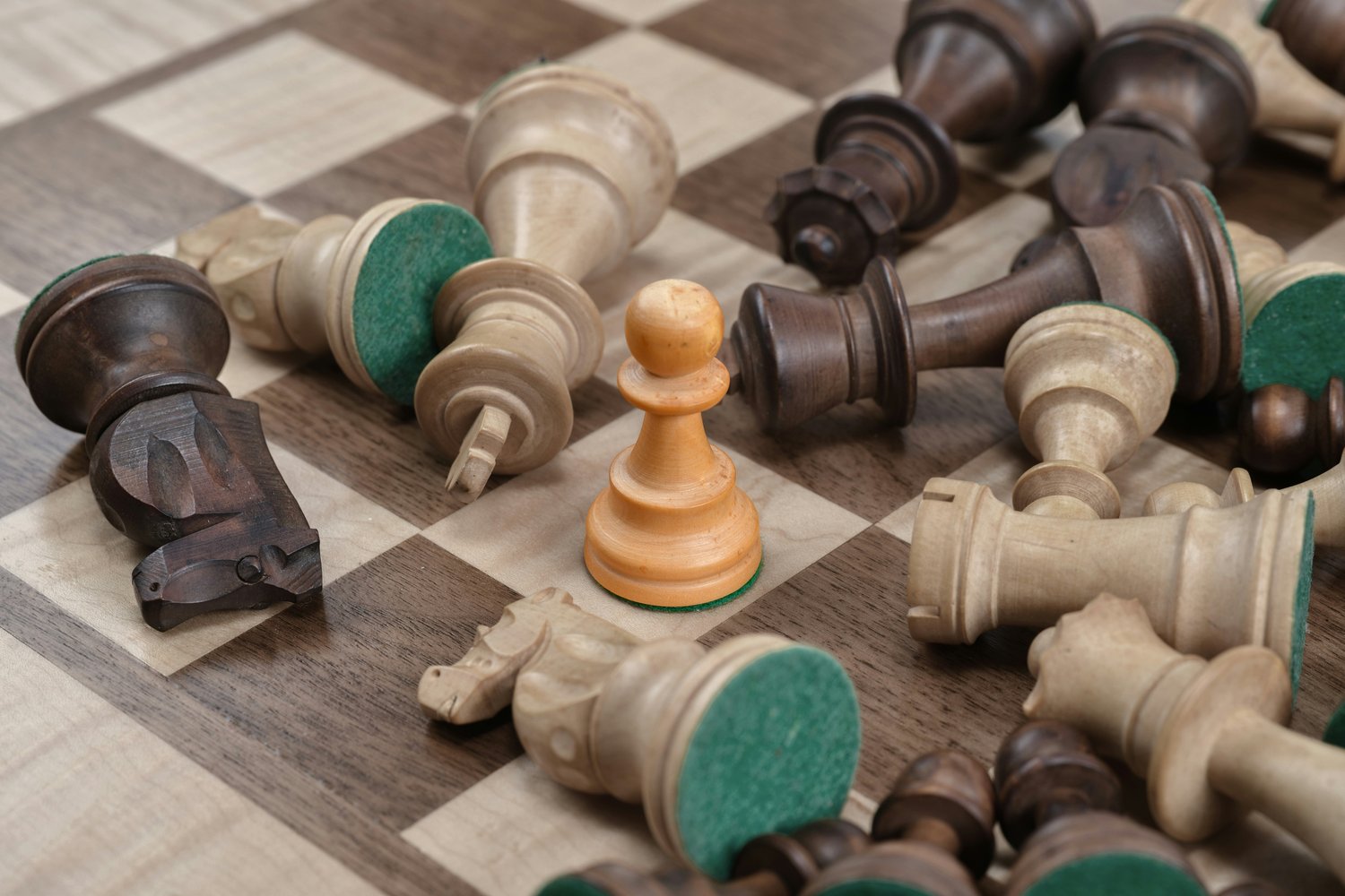 A close-up view of black and white chess pieces on a chess board. All the chess pieces are on their side, except one pawn which is upright in the middle of the image.