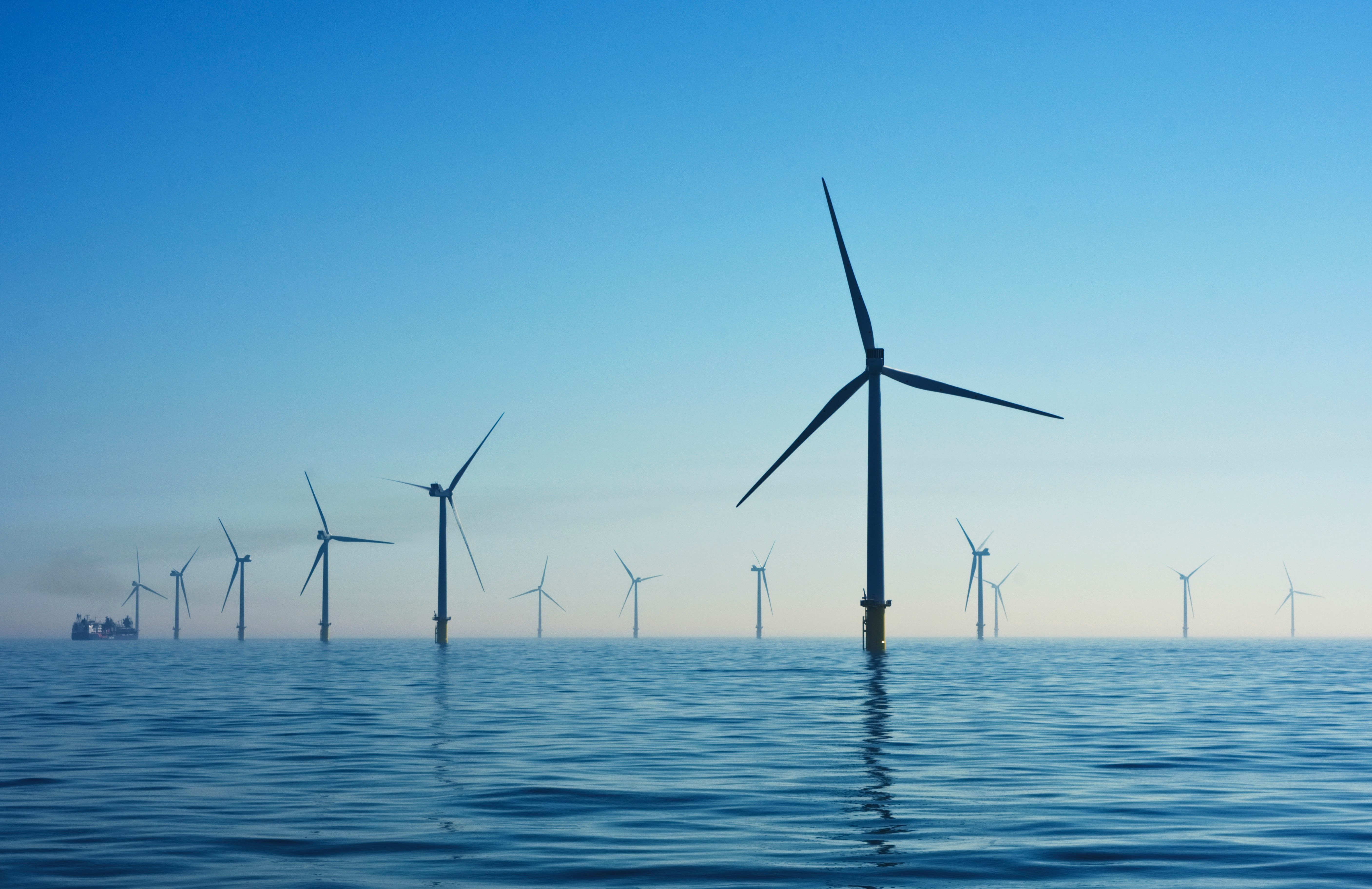 Photo of several wind turbines in the sea, pictured against a blue sky.